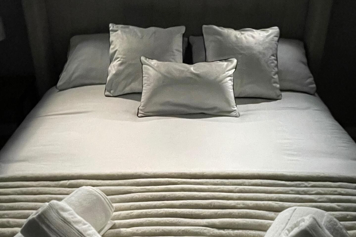 Un lit bien fait, avec une couette blanche, deux oreillers et une couverture pliée au pied du lit.