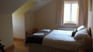 A bedroom with a bed, a window with curtains, a radiator, and a wooden floor.