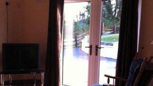 A living room with a television, a sofa, a wooden chair, and a sliding glass door leading to an outdoor area.