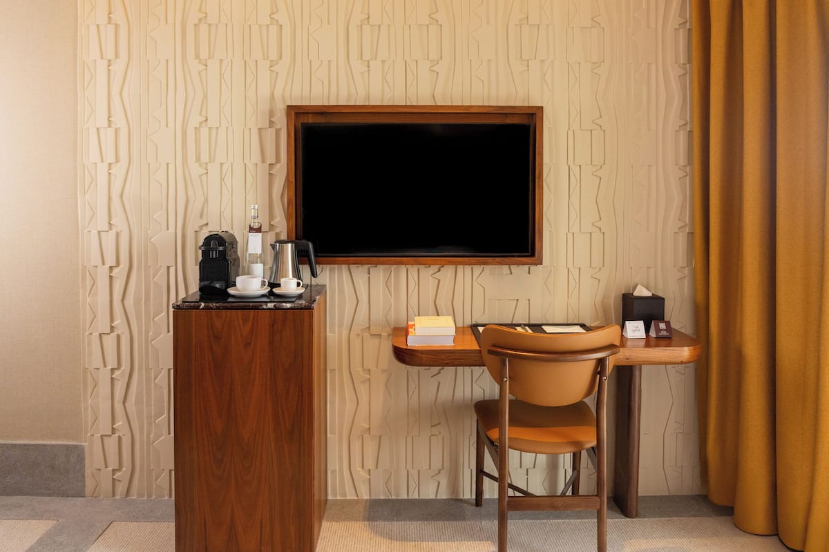 Habitación de hotel con un escritorio de madera, una silla, una cafetera, una taza, un libro y una caja de pañuelos.