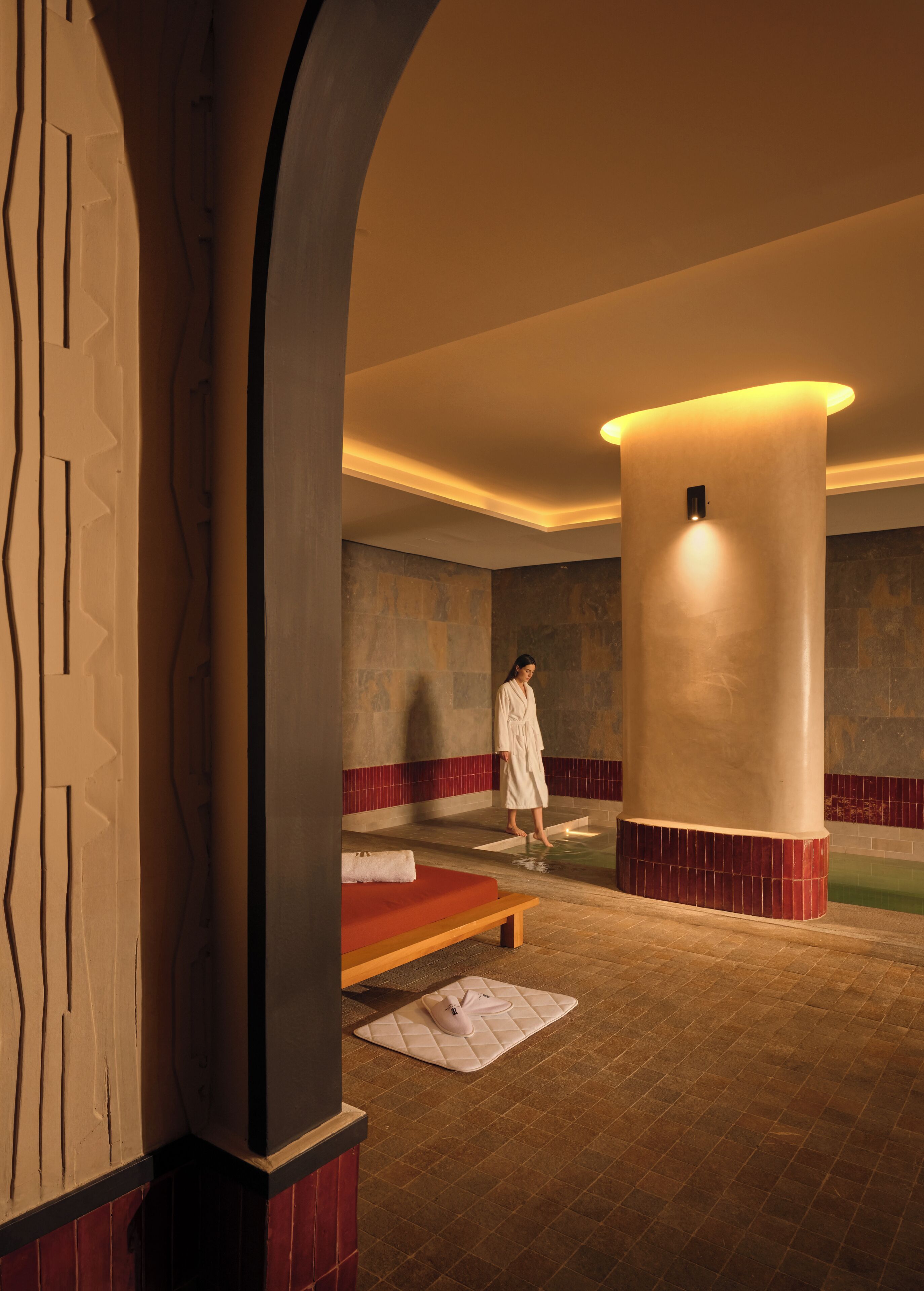 A spa room with a massage table, a bench, and a person in a robe.
