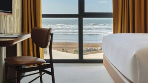 Ein Hotelzimmer mit großem Fenster, einem Bett, einem Sessel und einem Schreibtisch mit Fernseher.