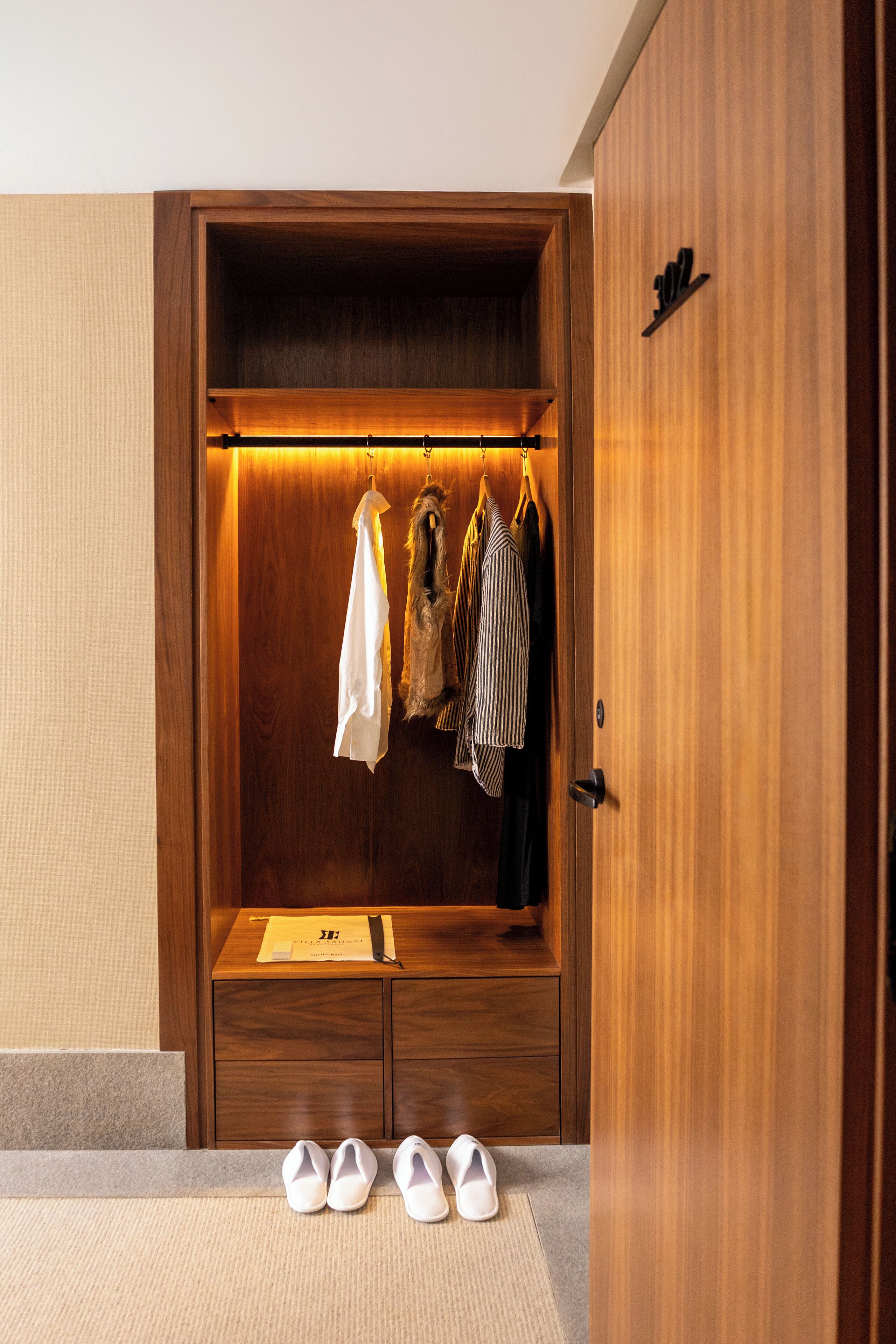 A wooden wardrobe with a hanging rack, a small table, and a pair of shoes on the floor.