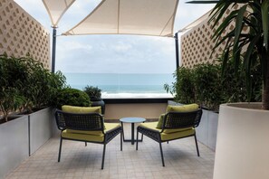A patio with two wicker chairs and a small table, overlooking the sea.