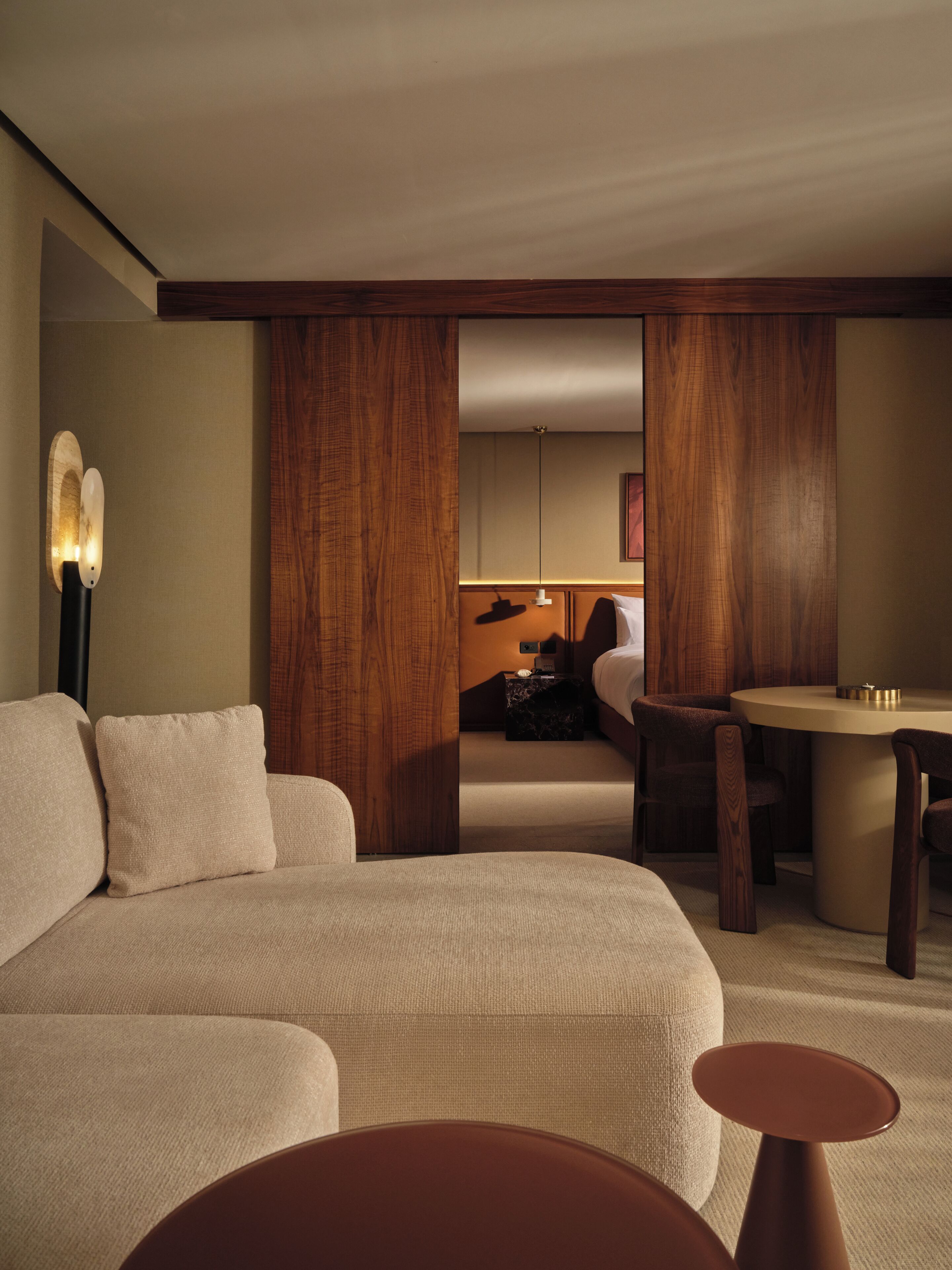 Una habitación de hotel moderna con un sofá grande, una mesita redonda pequeña, un escritorio y un espejo.