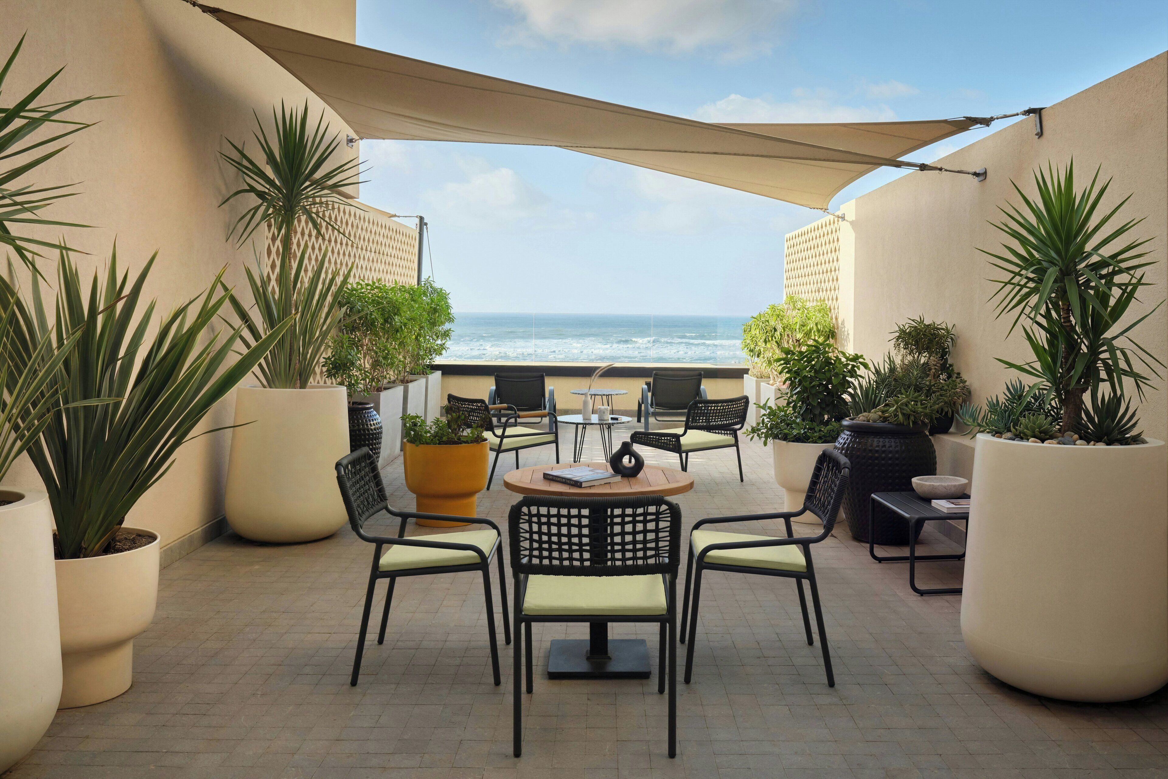 Um terraço com mesa e cadeiras, plantas em vasos e vista para o mar.