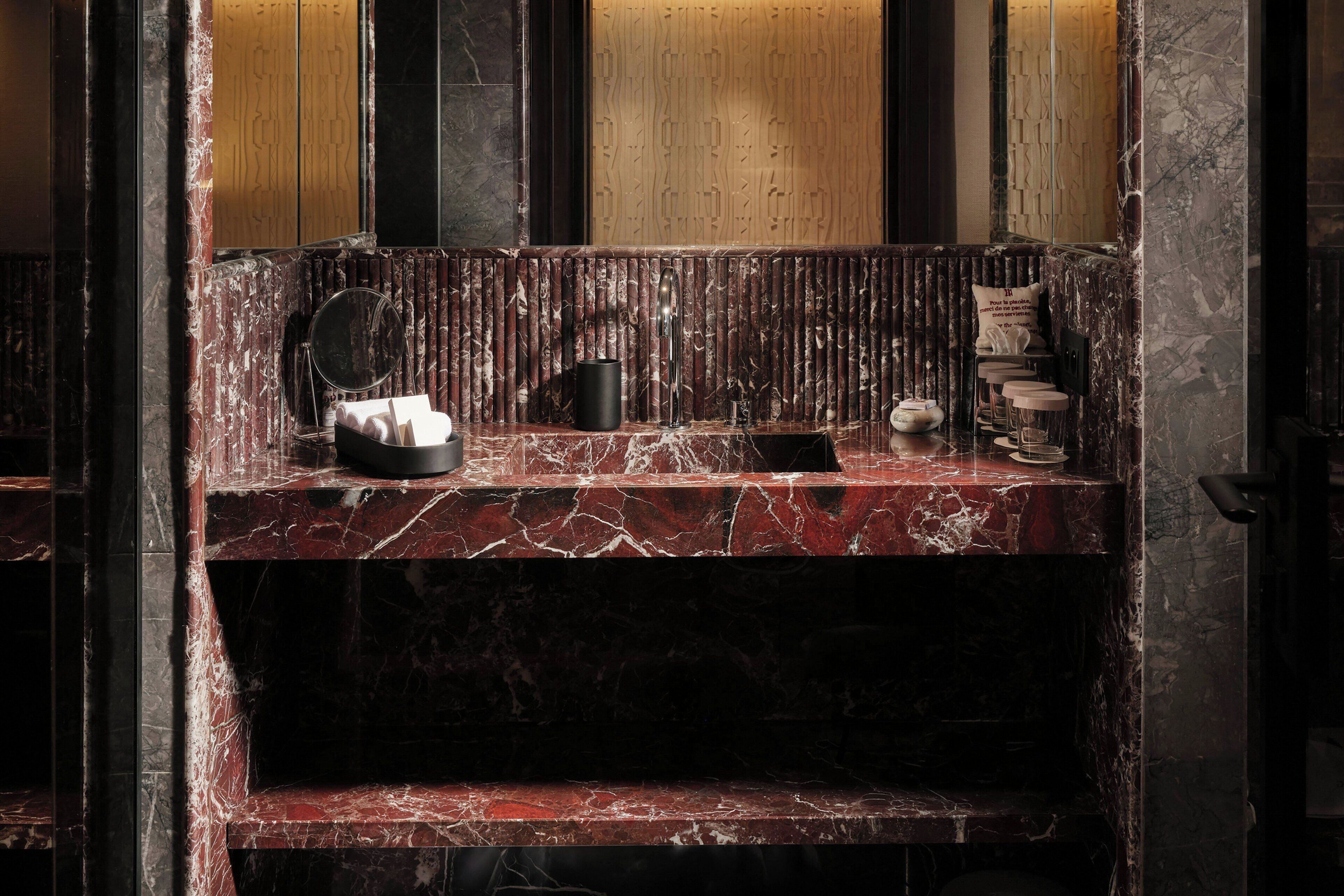 A bathroom with a marble vanity, a mirror, a black vase, and a towel rack.