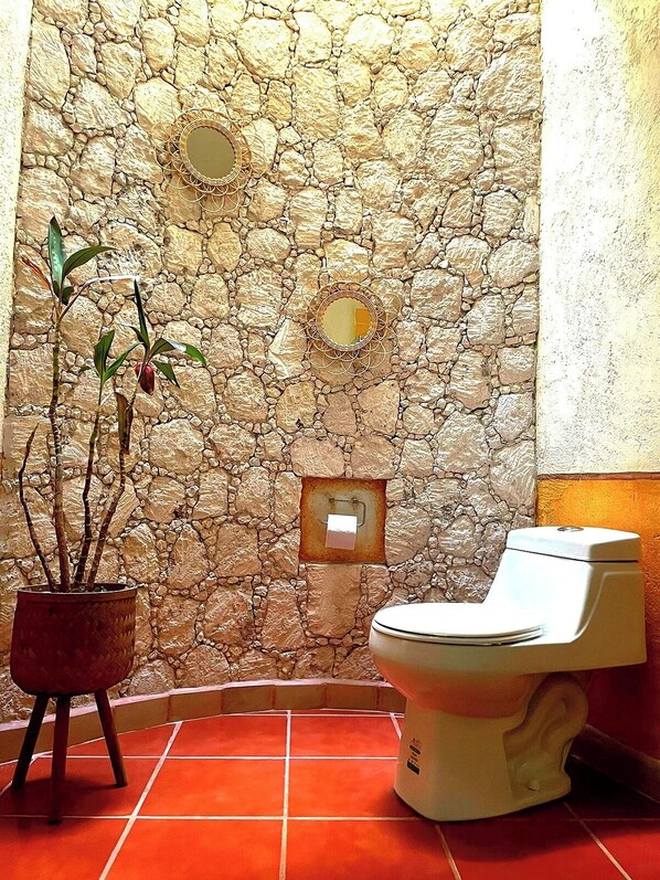 Ein Badezimmer mit Steinwand, Toilette, Topfpflanze und Spiegel.