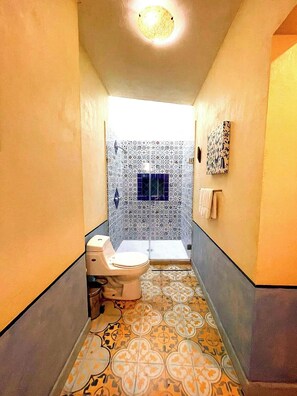 Ein schmaler Flur mit einer Toilette links und einer Duschkabine rechts, beide mit gemusterten Fliesen.