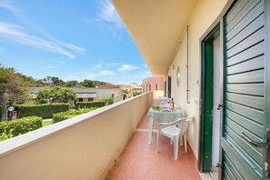 A balcony with a table and chairs, a green door, and a view of a garden and buildings. - Le Onde Apartment 4 with Pool n.114/b, Otranto, Italy (Otranto)