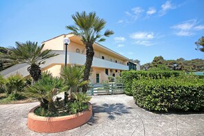 A building with a curved facade, palm trees, and a green fence. - Le Onde Apartment 4 with Pool n.114/b, Otranto, Italy (Otranto)