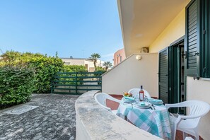Eine Terrasse mit einem für zwei Personen gedecktem Tisch, einem grünen Tor und einem Gebäude mit Fensterläden.