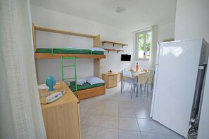 Ein kleines Zimmer mit Etagenbetten, einem Schreibtisch, einem Stuhl, einem Kühlschrank und einem Fenster mit Blick.