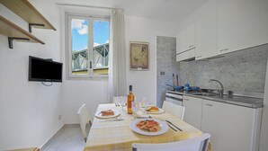 A small, bright kitchen with white cabinets, a dining table set with plates of food, and a window with a view of a bridge. - Le Onde Apartment 1 with Pool n.114/a, Otranto, Italy (Otranto)