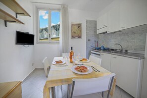 A small, bright kitchen with white cabinets, a dining table set with plates of food, and a window with a view of a bridge. - Le Onde Apartment 1 with Pool n.114/a, Otranto, Italy (Otranto)