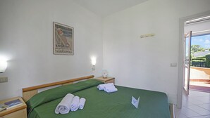 A hotel room with a bed, a nightstand, a poster on the wall, and a view of the outside. - Le Onde Apartment 1 with Pool n.114/a, Otranto, Italy (Otranto)