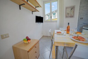 A dining area with a table set for two, a fruit bowl on a small wooden cabinet, and a television mounted on the wall.