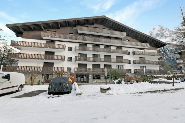 A multi-story building with balconies, a covered parking area, and snow on the ground.