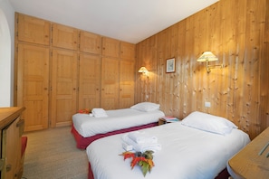 A hotel room with two beds, wooden panel walls, and a wall-mounted lamp.