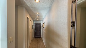 Un couloir avec un plancher en bois, des murs blancs et une porte au fond.
