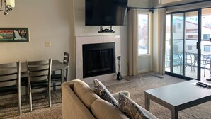 Un salon comprenant un canapé, une table à manger avec des chaises, une cheminée, un téléviseur à écran plat fixé au-dessus de la cheminée et une grande porte-fenêtre coulissante donnant sur un espace extérieur.