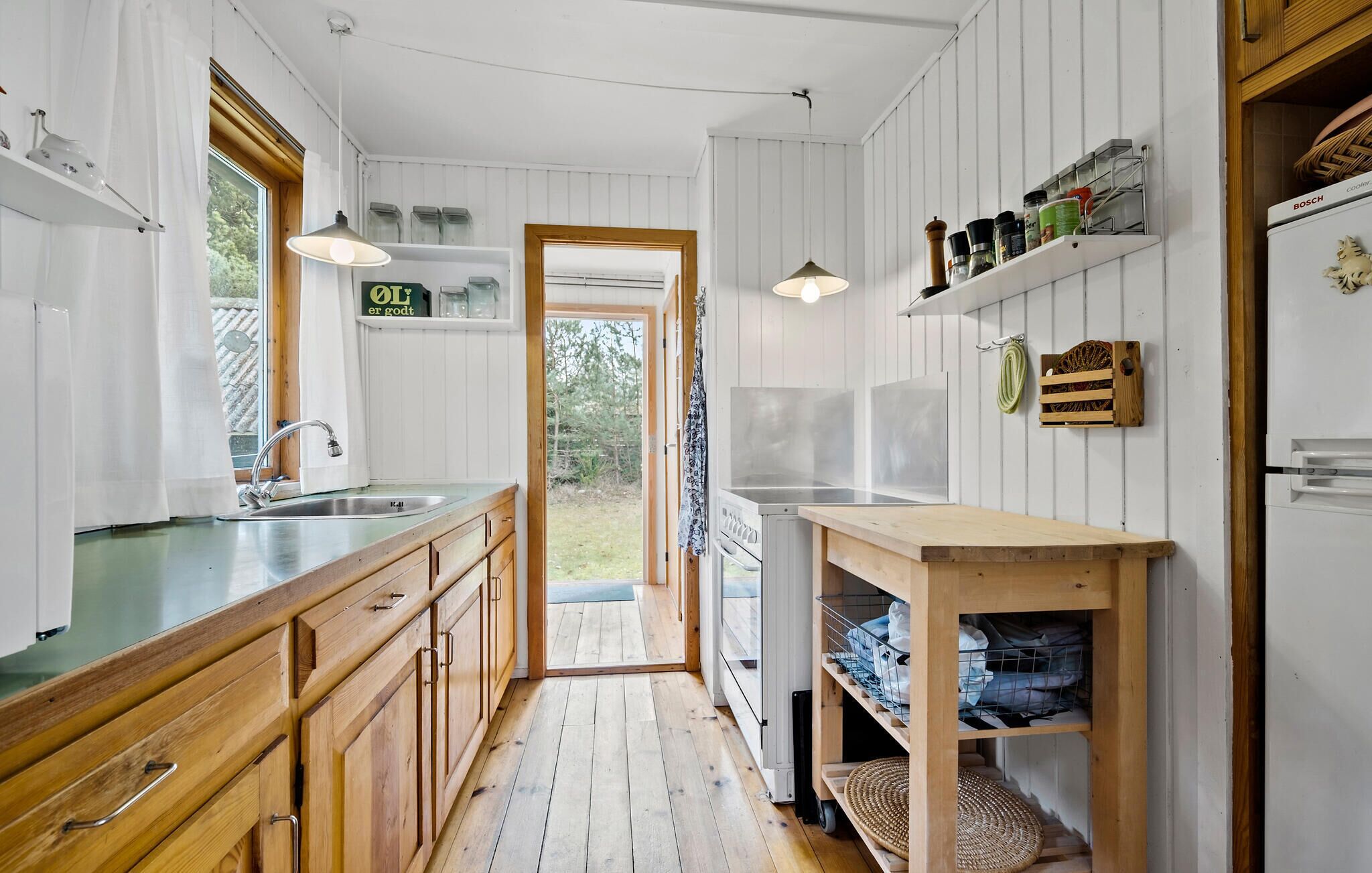 Une cuisine avec des meubles de rangement en bois, un évier, une cuisinière et un luminaire suspendu.