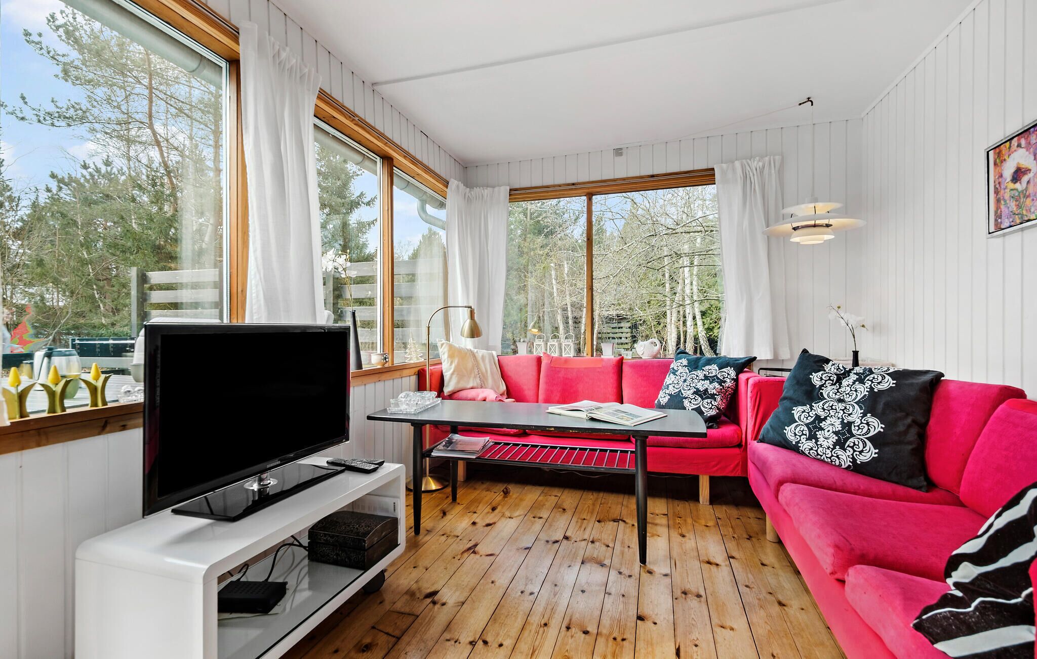 Un salon confortable avec un téléviseur, un canapé rouge et de grandes fenêtres.