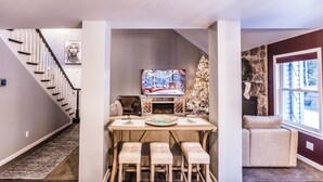 Un coin repas avec une table en bois, trois tabourets de bar, un sapin de Noël et une cheminée.