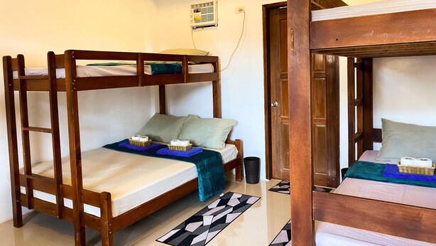 A room with two bunk beds, a small window, a wall-mounted air conditioner, and a tiled floor. - Hapitanan Siargao (General Luna)