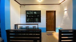 A room with a wooden bench, a table with three stools, a door, and a window with a geometric pattern. - Hapitanan Siargao (General Luna)