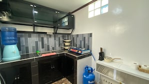 A kitchen with a gas stove, a water dispenser, a sink, and a gas cylinder. - Hapitanan Siargao (General Luna)