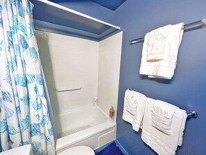 A bathroom with a bathtub, a shower, and a toilet. There are towels hanging on a rack and a curtain with a leaf pattern. - Simple Studio 1 block from Beach (Honolulu)
