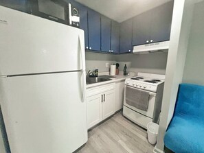 A compact kitchen with a refrigerator, stove, sink, and cabinets. - Simple Studio 1 block from Beach (Honolulu)