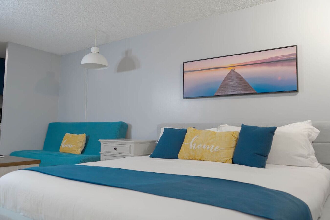 Un dormitorio con una cama, una mesita de noche, un sofá azul y un cuadro colgado en la pared.