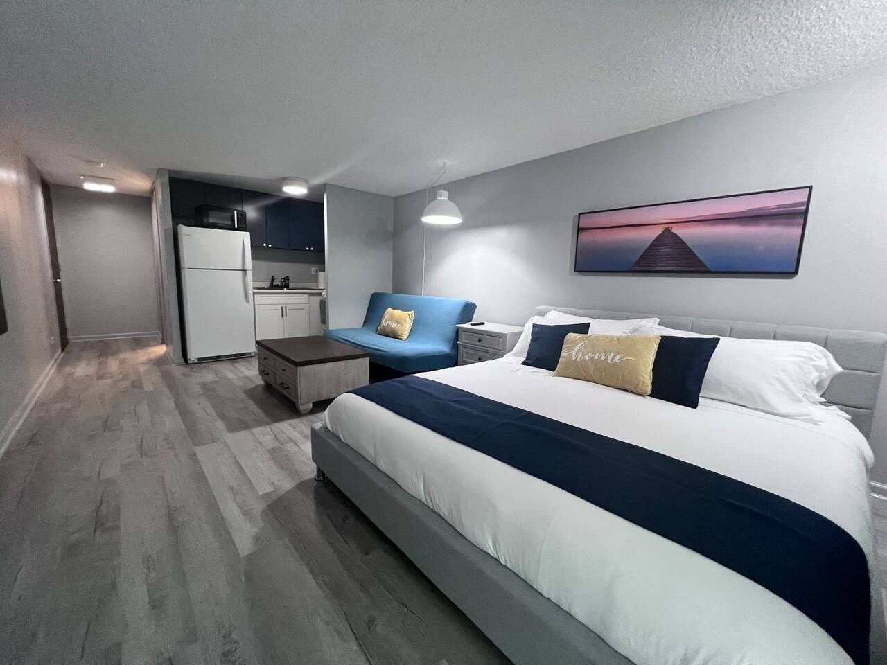 Quarto moderno com cama grande, escrivaninha e cozinha compacta.
