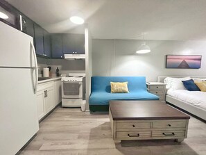 A compact living space with a kitchenette, a sofa, a bed, and a small table. - Simple Studio 1 block from Beach (Honolulu)