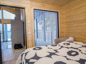 A wooden room with a bed, a suitcase, and a sliding door leading to a balcony. - Lakeside villa by Interhome (Nurmes)