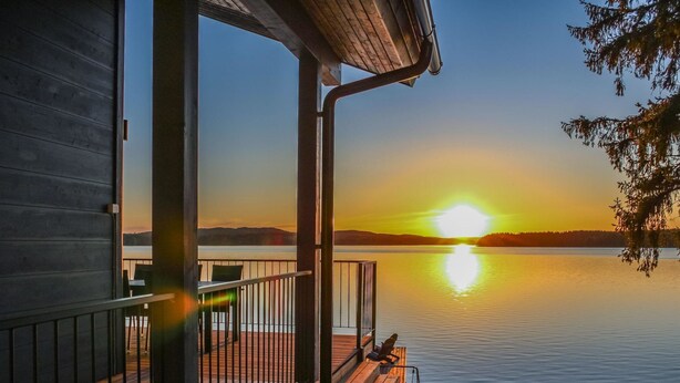 A wooden deck with a railing overlooking a calm lake at sunset. - Lakeside villa by Interhome (Nurmes)
