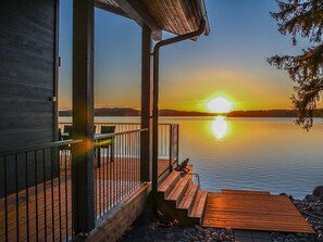 A wooden deck with a railing overlooking a calm lake at sunset. - Lakeside villa by Interhome (Nurmes)