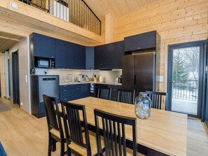 A modern kitchen with dark cabinetry, stainless steel appliances, and a dining area with wooden furniture.