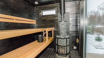 Un sauna avec des bancs en bois, un poêle en pierre et une fenêtre donnant sur un paysage enneigé.