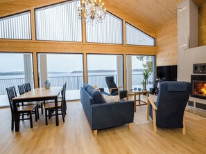 A spacious living area with a high ceiling, large windows, a fireplace, and a view of a body of water.