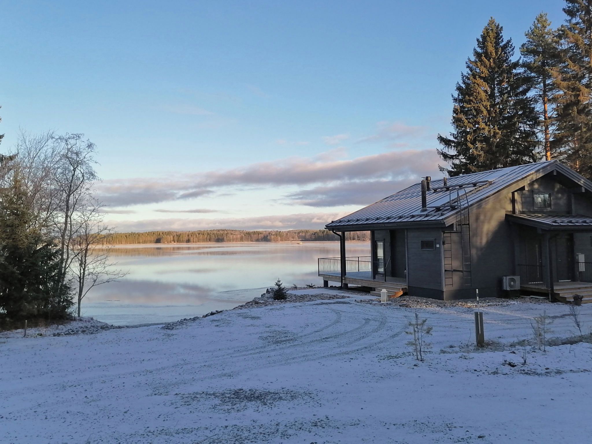 A cabin with a dock extending into a frozen lake, surrounded by snow and trees.