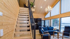 A wooden interior with a staircase, a living area with a sofa and chairs, and large windows offering a view. - Lakeside villa by Interhome (Nurmes)