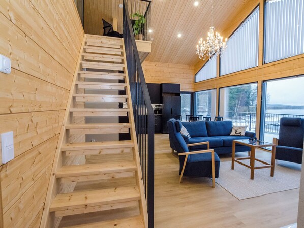 A wooden interior with a staircase, a blue sofa set, and large windows.