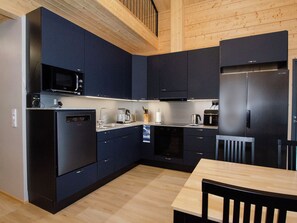 A modern kitchen with dark cabinetry, a microwave, a refrigerator, and a dining table with chairs. - Lakeside villa by Interhome (Nurmes)