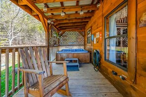 A wooden deck with a hot tub, two Adirondack chairs, and a covered area with a lattice window.