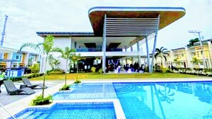 Un edificio moderno con zona de piscina, incluyendo sillas de descanso y una piscina azul cristalina.