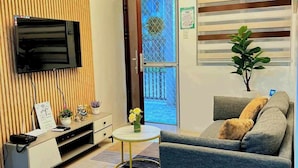 Una sala de estar moderna con un televisor de pantalla plana, un sofá, una pequeña mesa redonda y una planta decorativa.