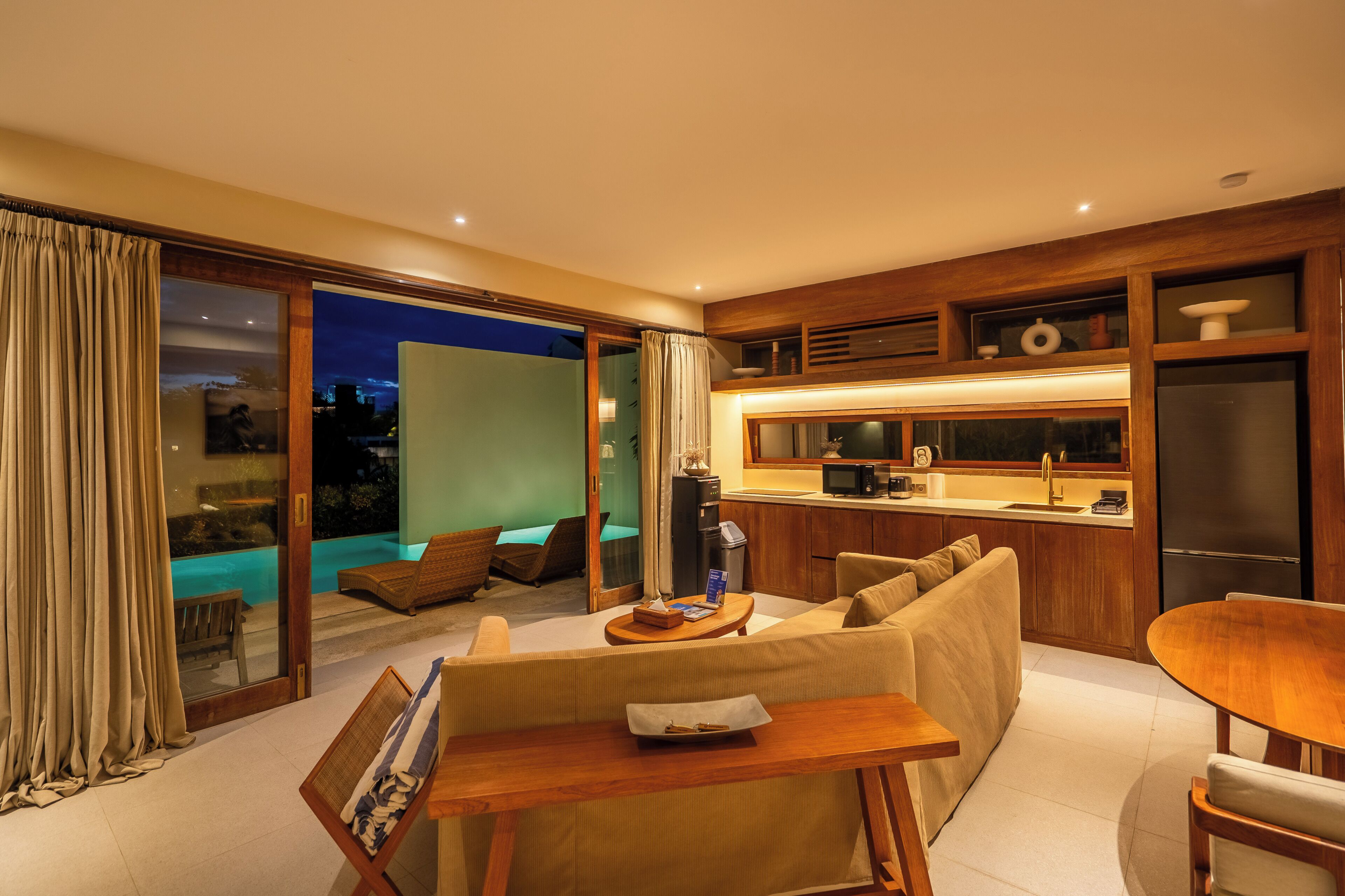 A modern living room with a sofa, a dining table, and a kitchen area with a refrigerator and microwave.